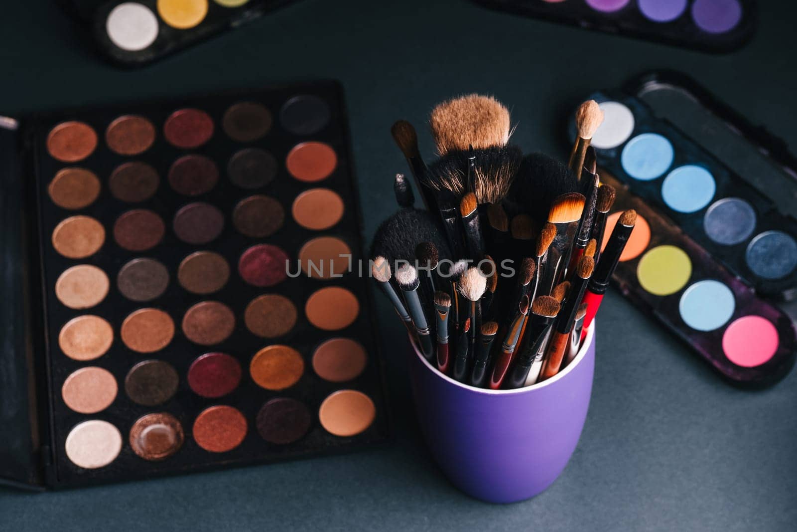 set of professional makeup brushes on a palette background with colored eye shadows on the table