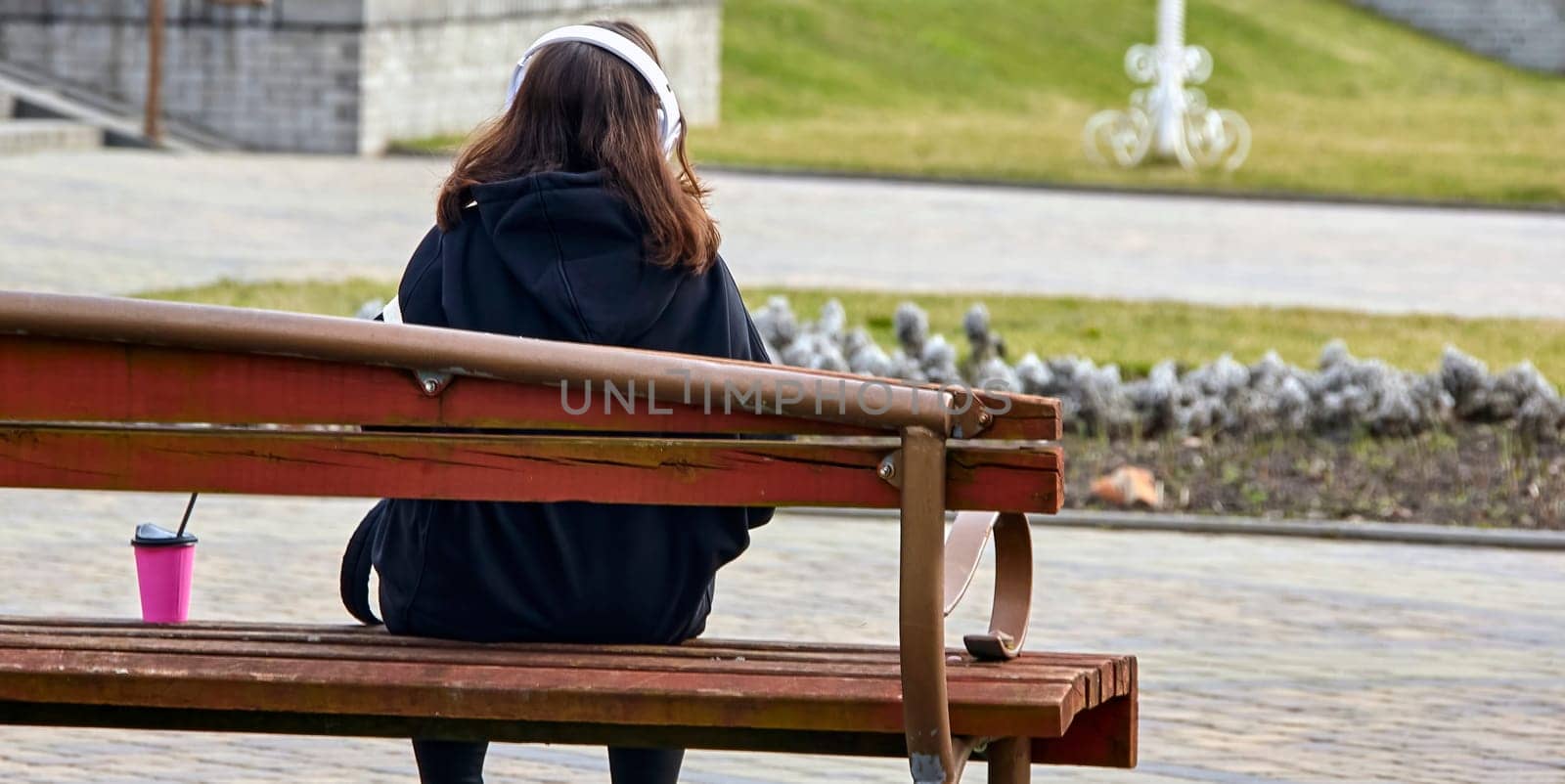 A thoughtful and serene young woman, casually dressed, takes a moment to relax and reflect on a park bench. Pigeons wander nearby as the urban cityscape forms a backdrop to her contemplative mood.