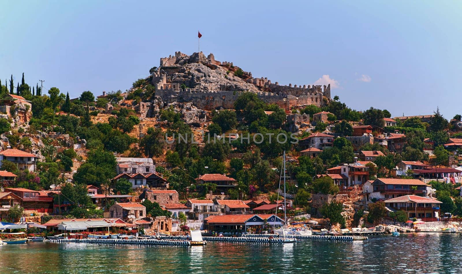 Charming Mediterranean village on Turkish coast with red-roofed houses, historic stone castle, and stunning sea views, perched on cliffs overlooking the azure waters of the Mediterranean Sea.