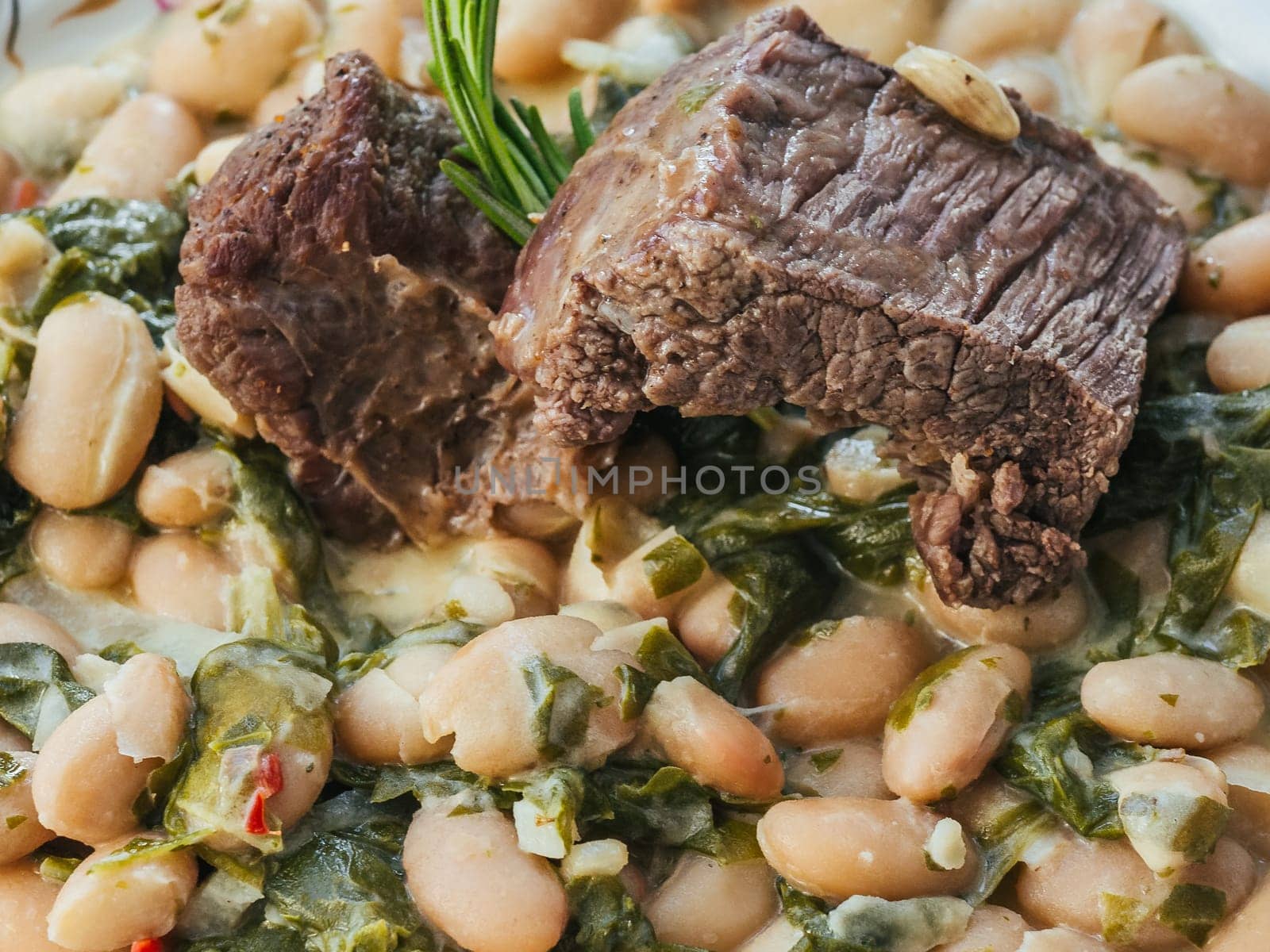cooked beef in a sauce with beans and rosemary close-up