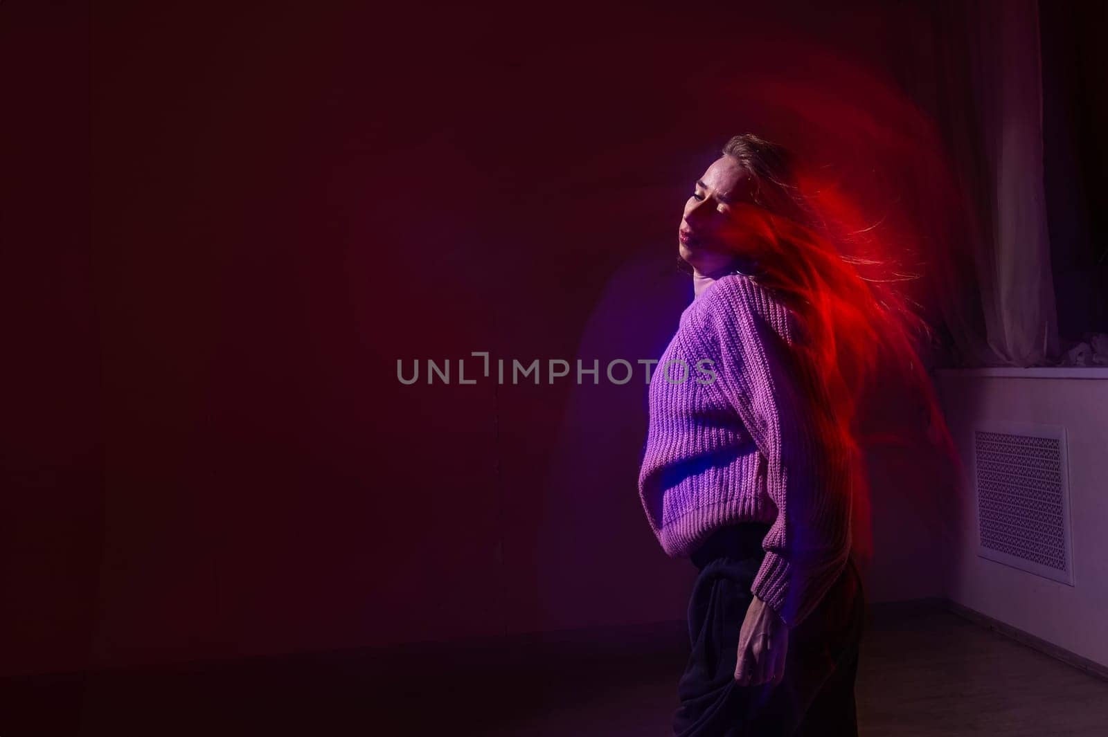 A young woman dances contemporary dances in blue and red light. Long exposure photo
