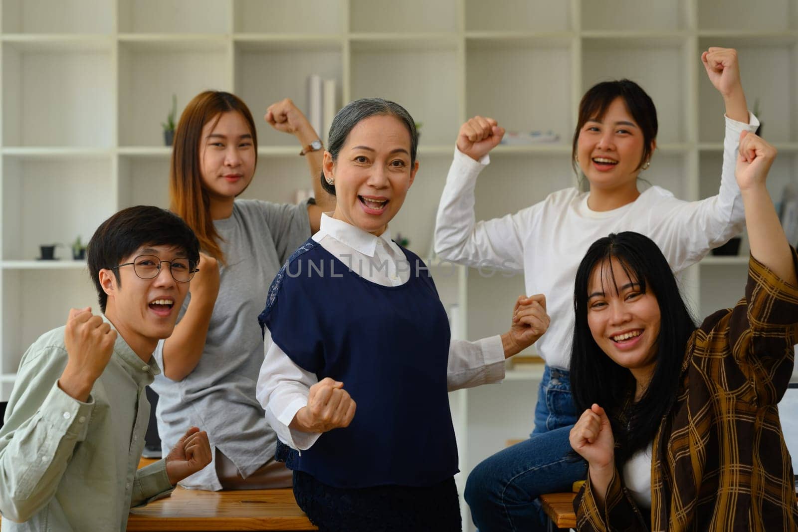 Group of happy university students and mature professor celebrating success in the classroom.