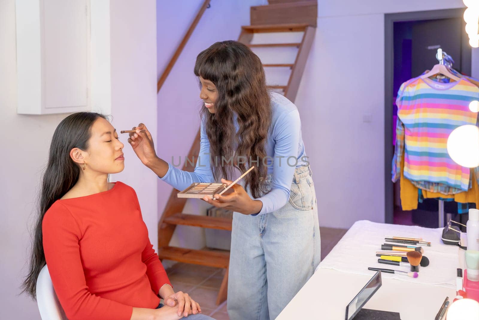 Makeup artist applying makeup to woman's face in front of a mirror. People together having fun. High quality photo