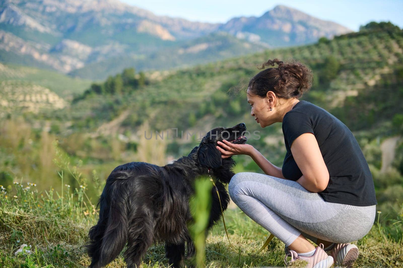 Affectionate young woman embracing her pedigree black cocker spaniel pet dog while walking him in the mountains nature. Playing pets and people concept by artgf
