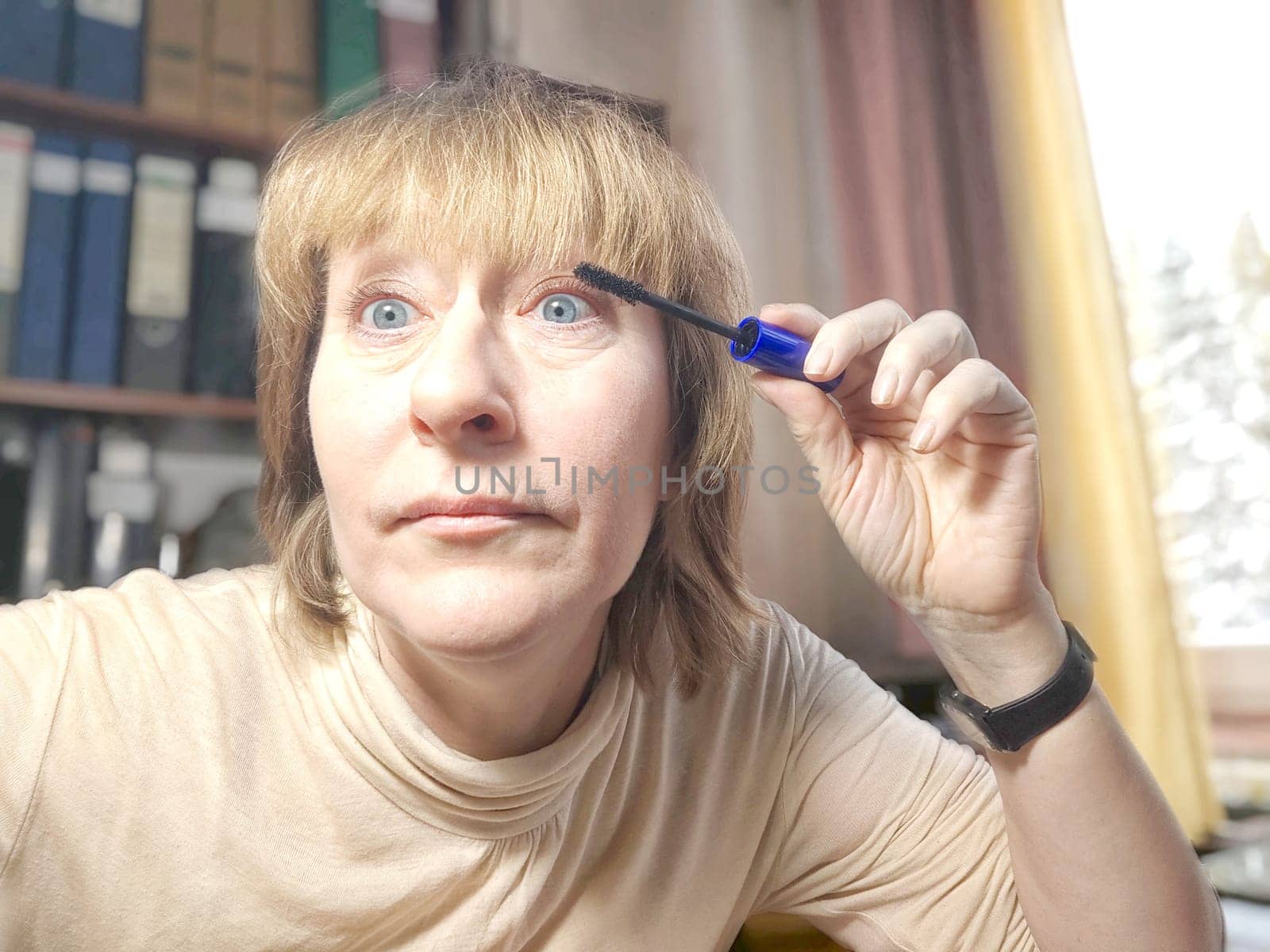 Portrait of a middle-aged woman doing eye makeup. Selfie portrait of a lady who is businesswoman, accountant, manager, freelancer doing morning makeup at office on working place by keleny