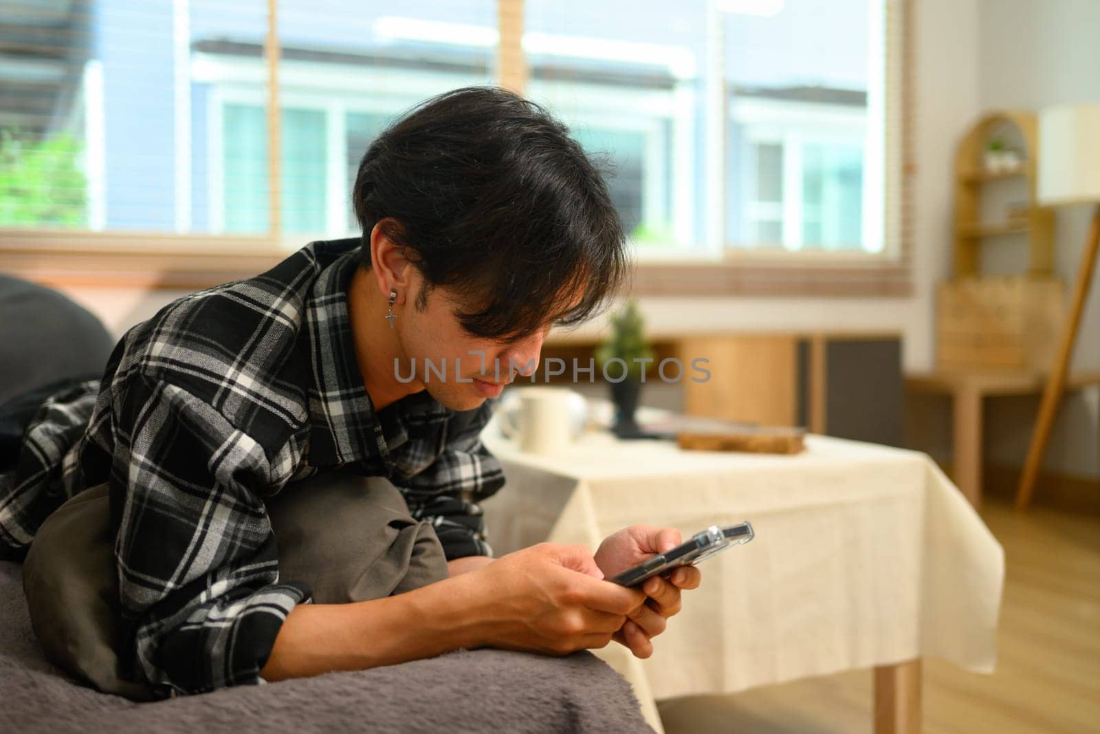 Relaxed young man lying on couch and typing text message on mobile phone.