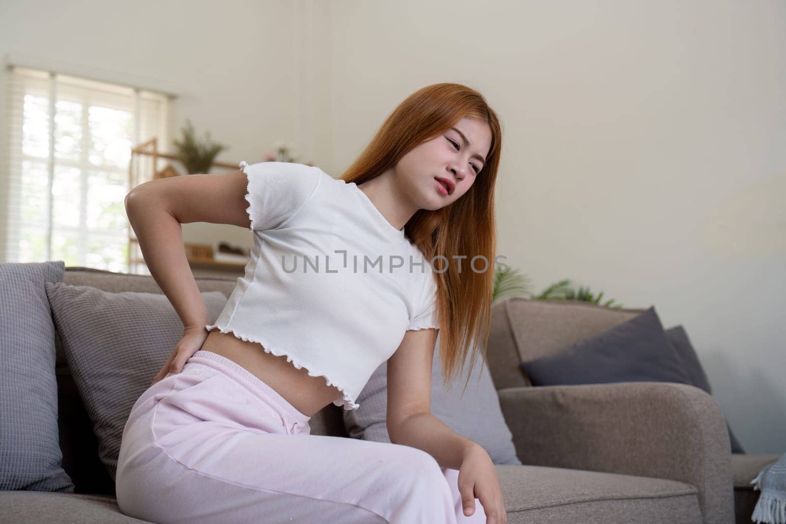 Asian woman having backache and touching her back in living room at home by nateemee