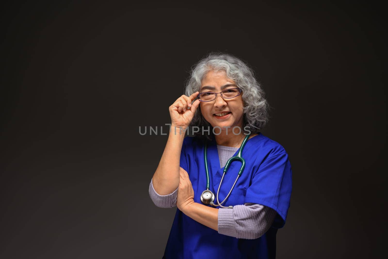 portrait of senior doctor woman in eyeglasses standing on black background looking confident at the camera.