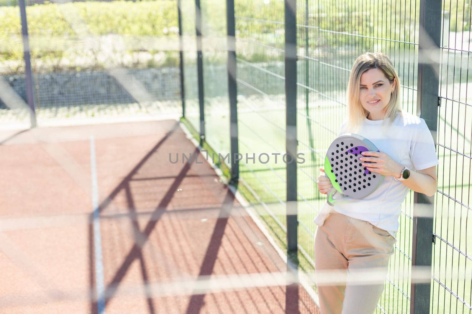 Happy female paddle tennis player during practice on outdoor court looking at camera. Copy space. by Andelov13