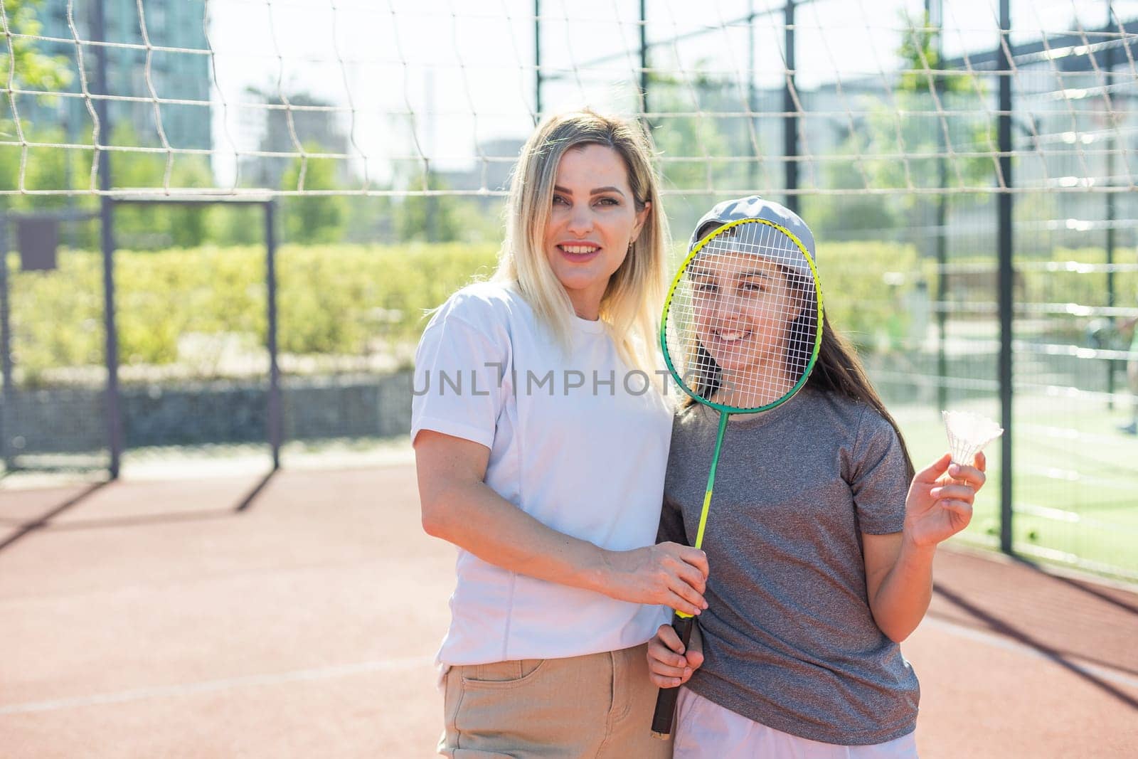 Mother and daughter are playing badminton outside in the yard on summer hot day by Andelov13