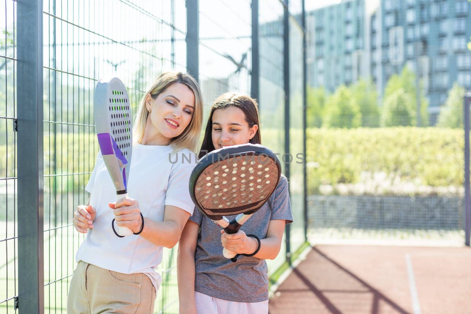 Cheerful coach teaching child to play padel tennis while both standing on tennis court. High quality photo