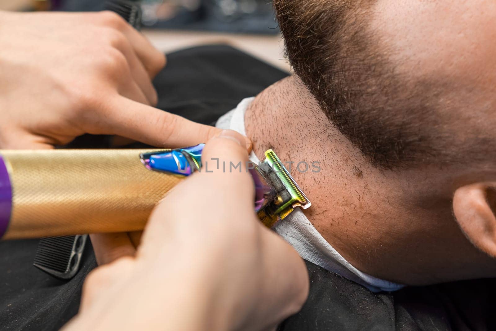 At the barbershop, the master effortlessly trims the clients beard using an automatic trimmer