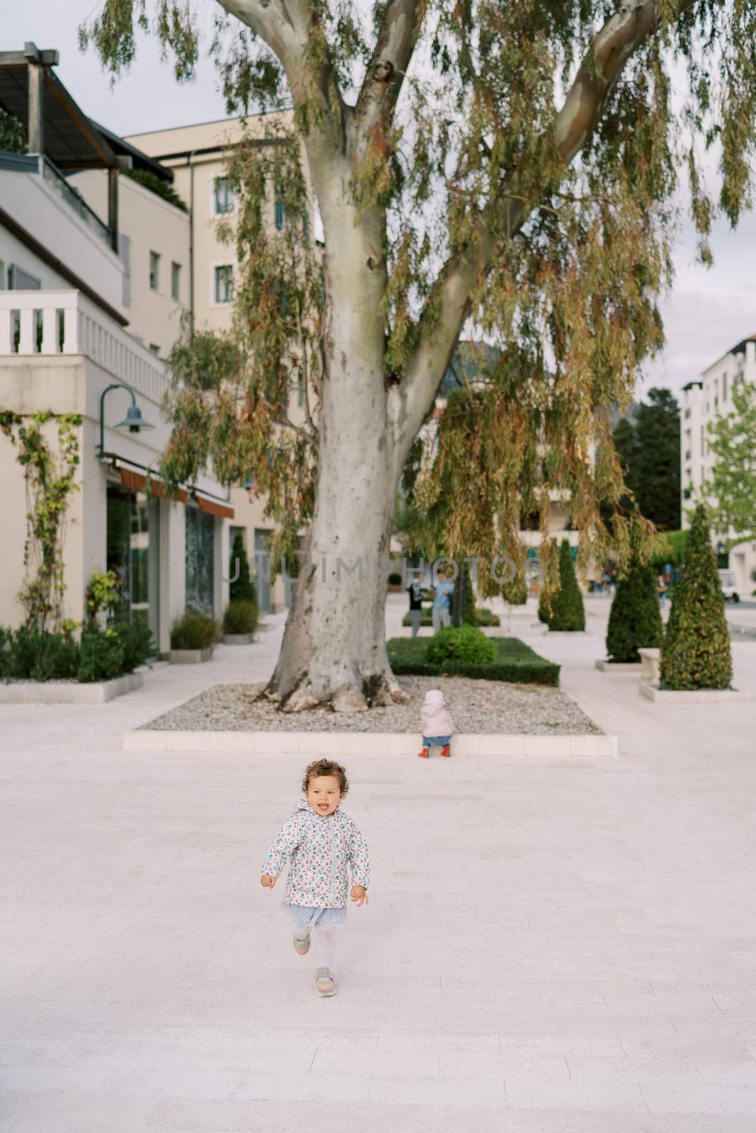 Little girl runs along the road near apartment buildings. High quality photo