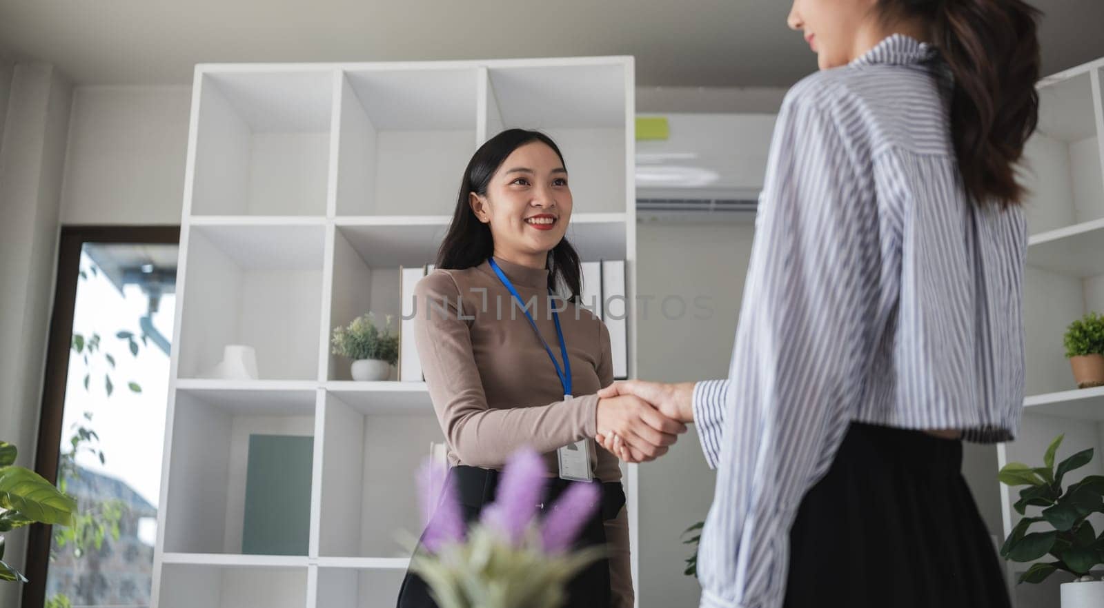 Two Asian businesswomen shaking hands in the office. Concept of partnership and agreement by wichayada