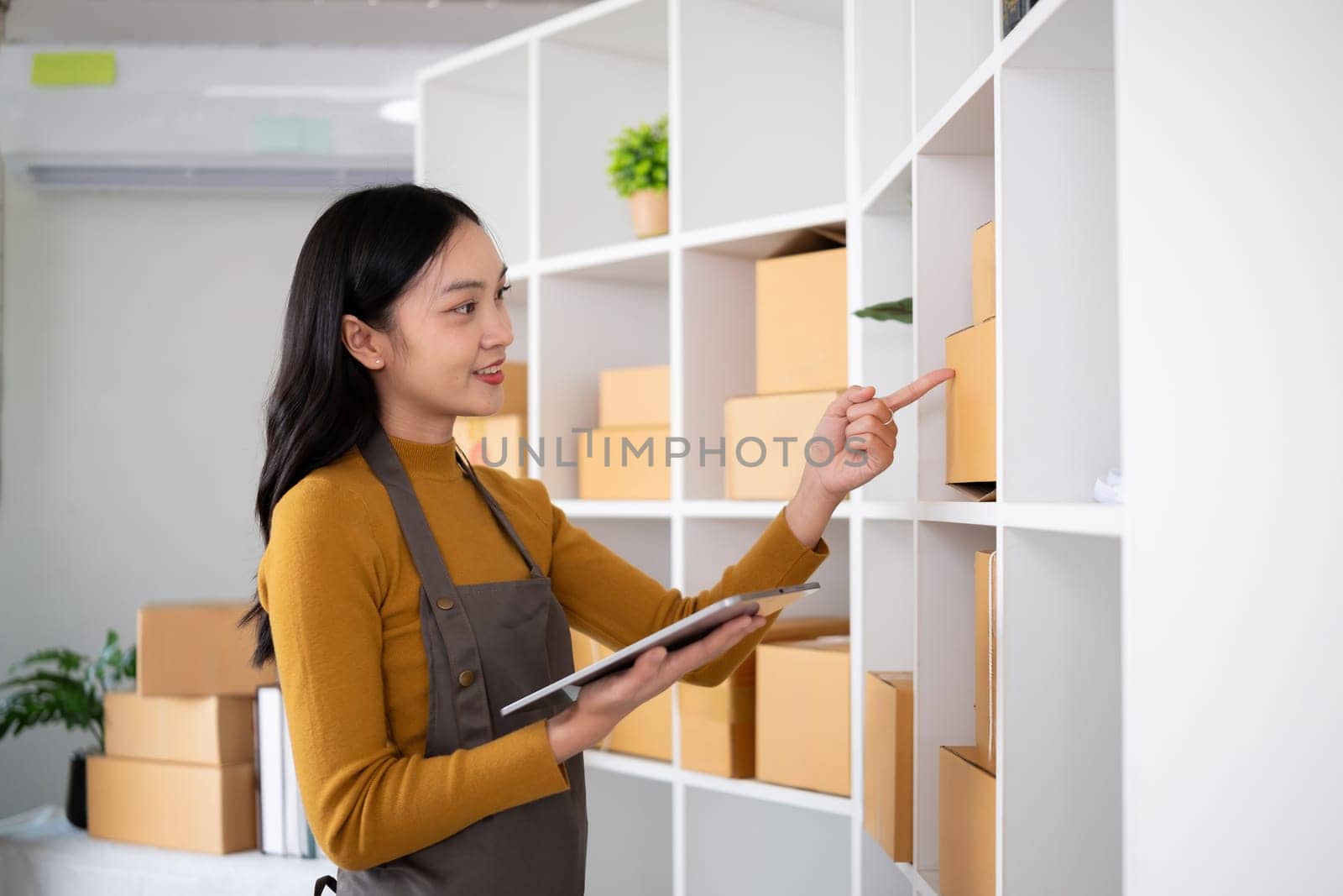 Young woman working in warehouse with packages using tablet for inventory management.