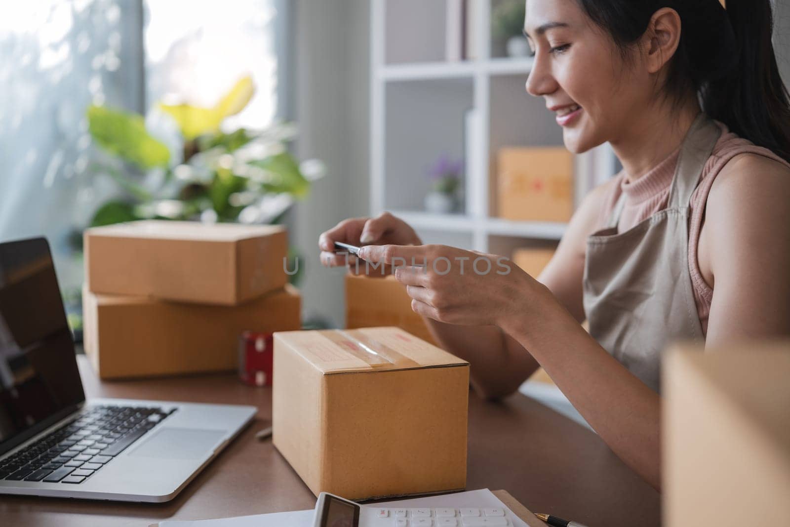 Smiling young woman in warehouse scanning package with smartphone.