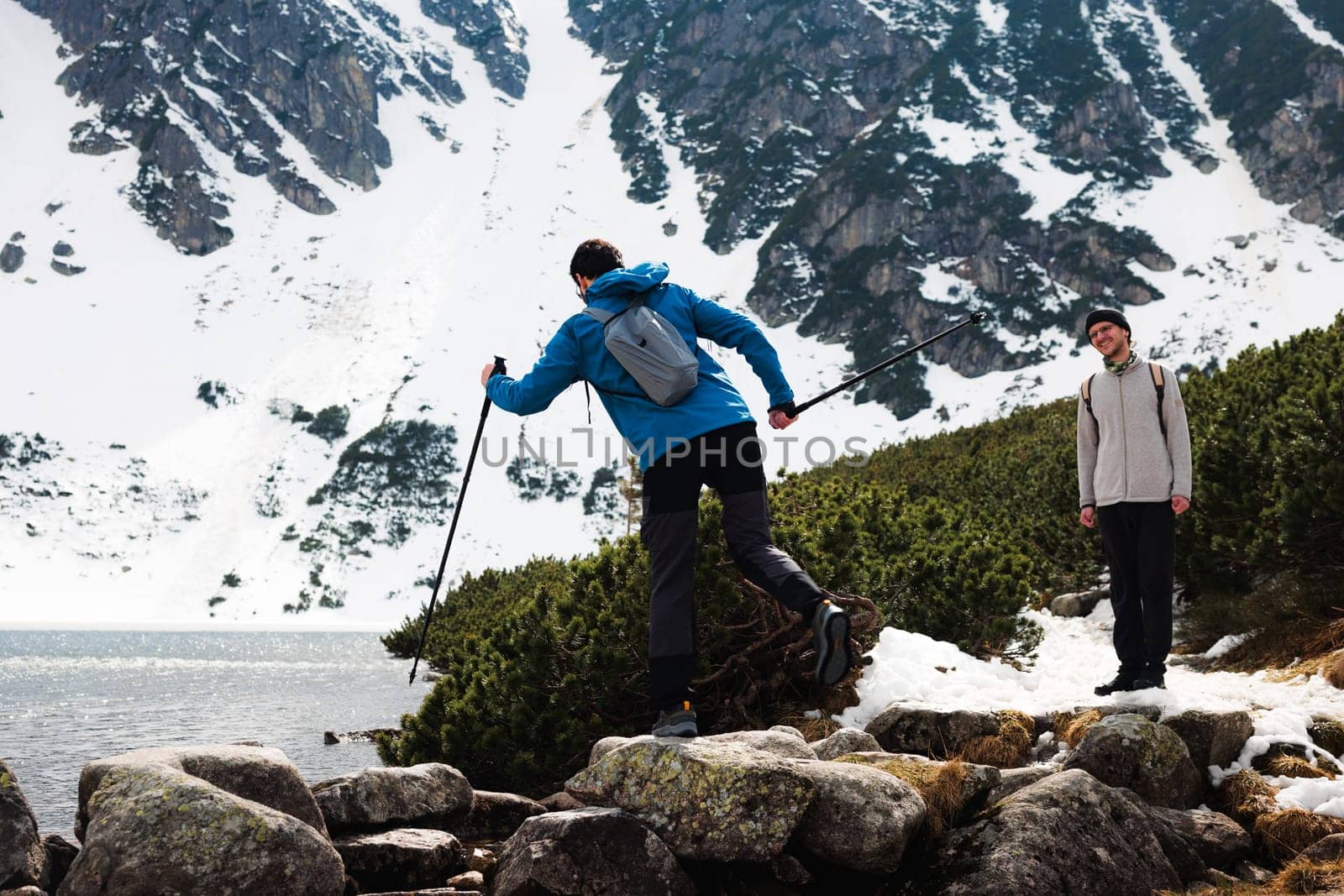 Two friends are trekking through the snowy mountains, enjoying the natural landscape and water views near a highland lake