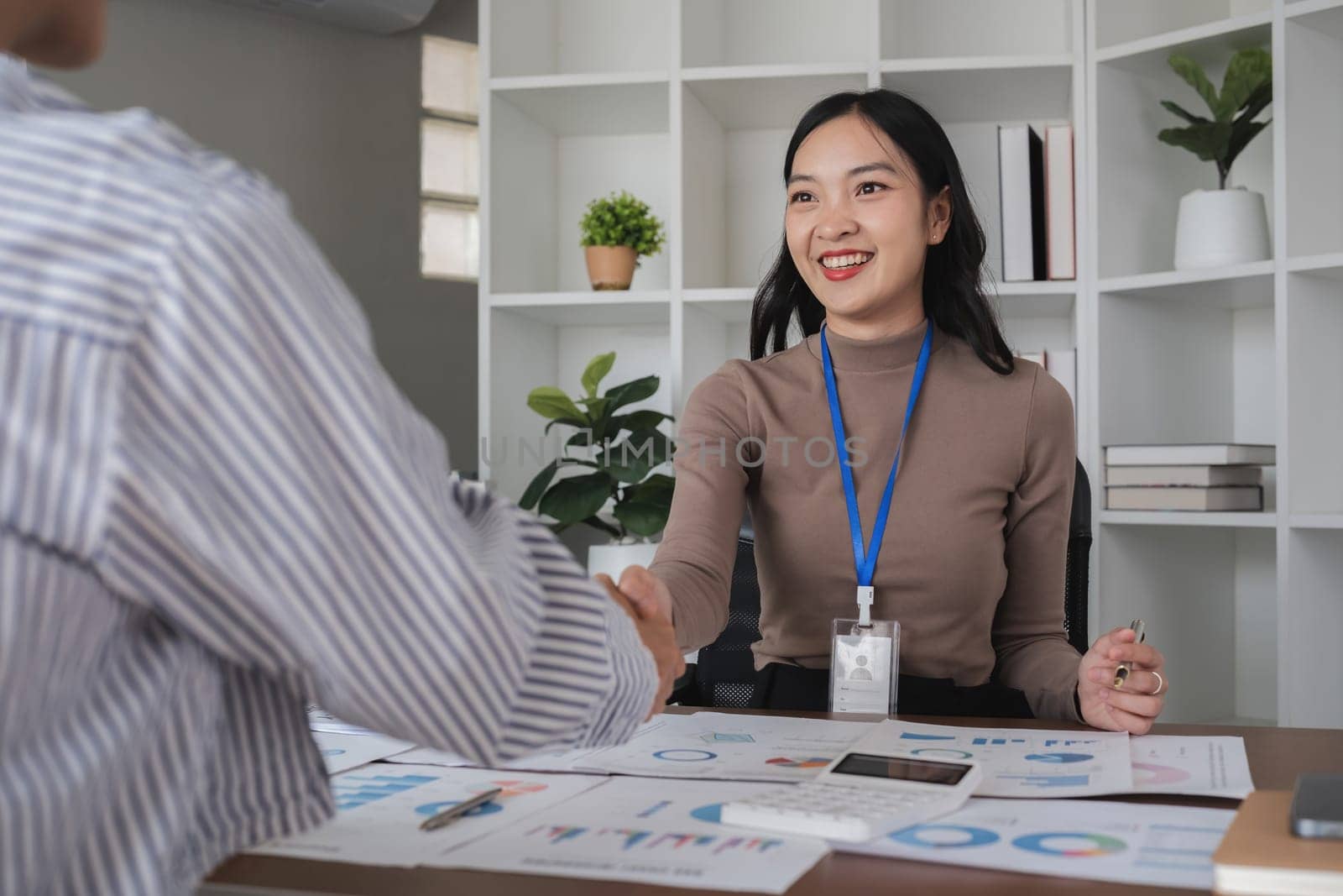 Two Asian businesswomen shaking hands in the office. Concept of partnership and agreement by wichayada