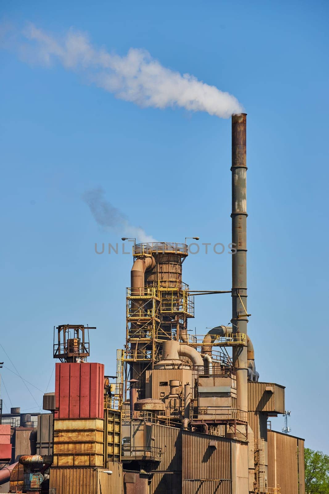 Industrial facility in Warsaw, Indiana, with a towering chimney emitting smoke against a clear blue sky.