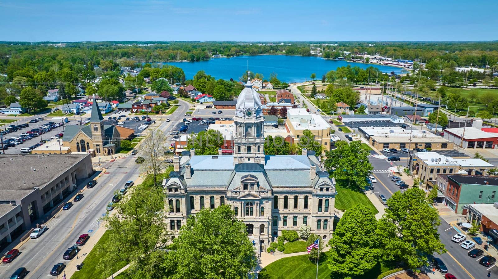 Aerial view of Warsaw, Indiana, showcasing the historic Kosciusko County Courthouse surrounded by lush greenery and serene lake.