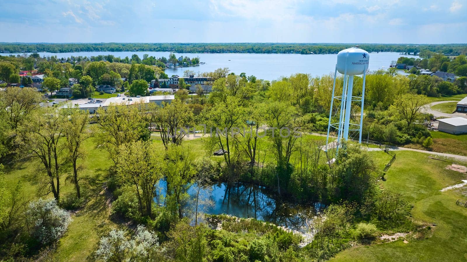 Aerial view of Warsaw, Indiana showcasing lush parkland, a striking American water tower, and serene Winona Lake.