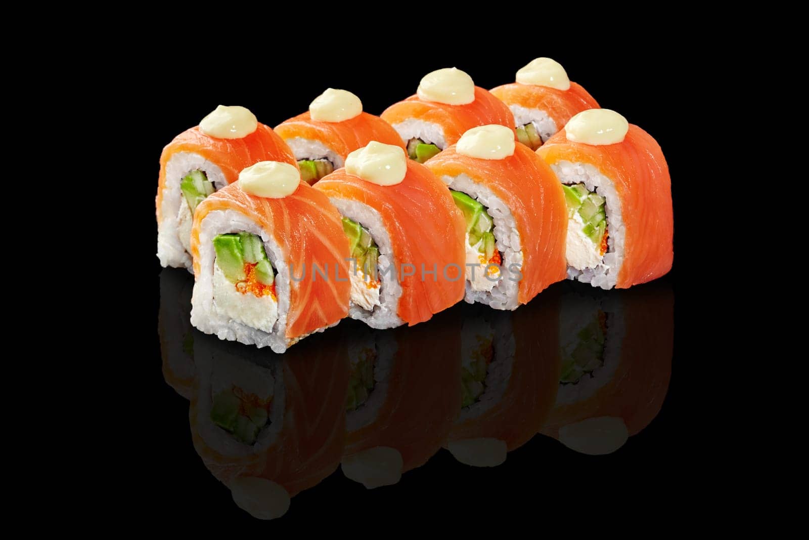 Classic Japanese sushi rolls filled with avocado, tobiko and cream cheese topped with fresh salmon slices and drops of mayo, presented on glossy reflective black background