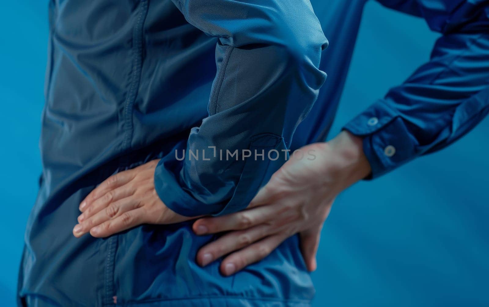 A person in pain, clutching their lower back. The image uses a clinical blue tone to symbolize chronic back pain and discomfort. by sfinks