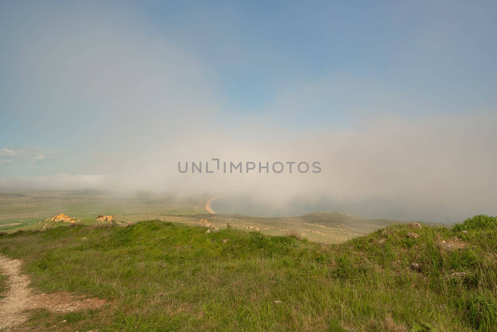 A foggy day with a cloudy sky and a grassy hill. The sky is blue and the clouds are white