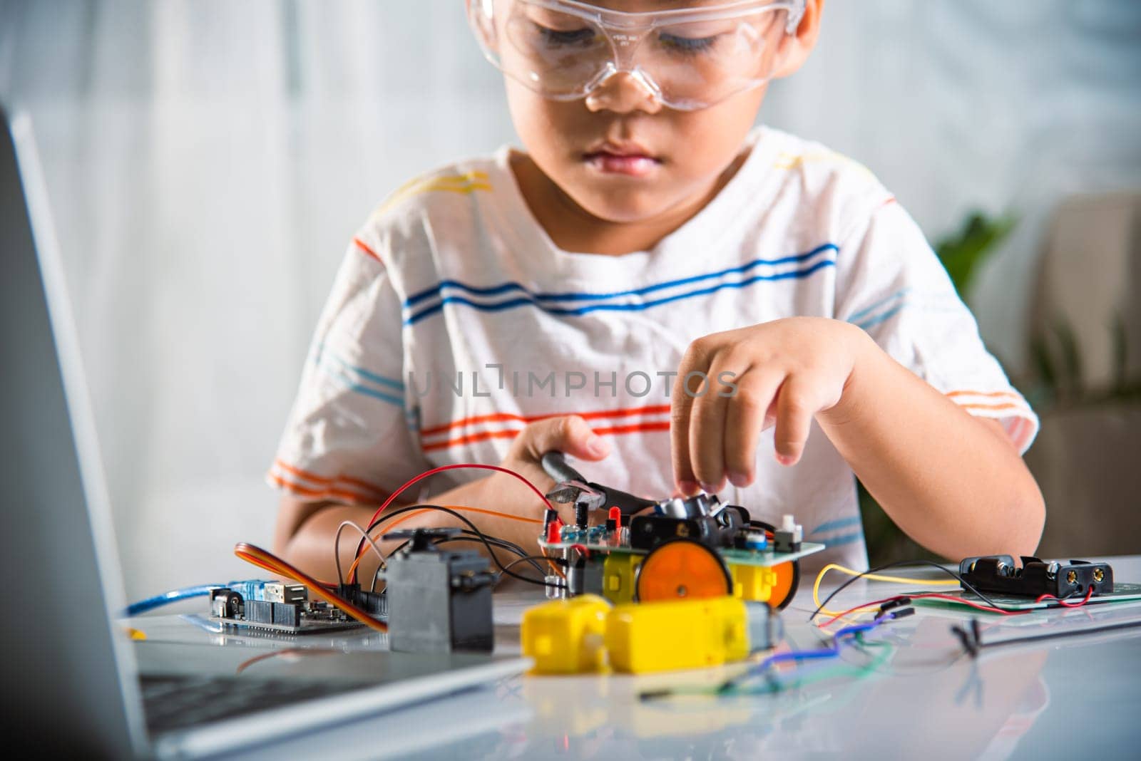 Little child tighten the nut with a screwdriver to assemble car toy, Asian kid boy assembling the Arduino robot car homework project at home, education AI technology workshop school learning lesson