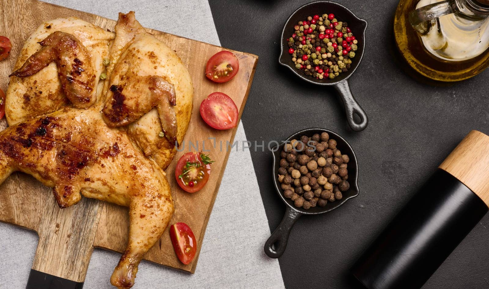 Whole fried chicken with spices on a wooden board on a black table, top view