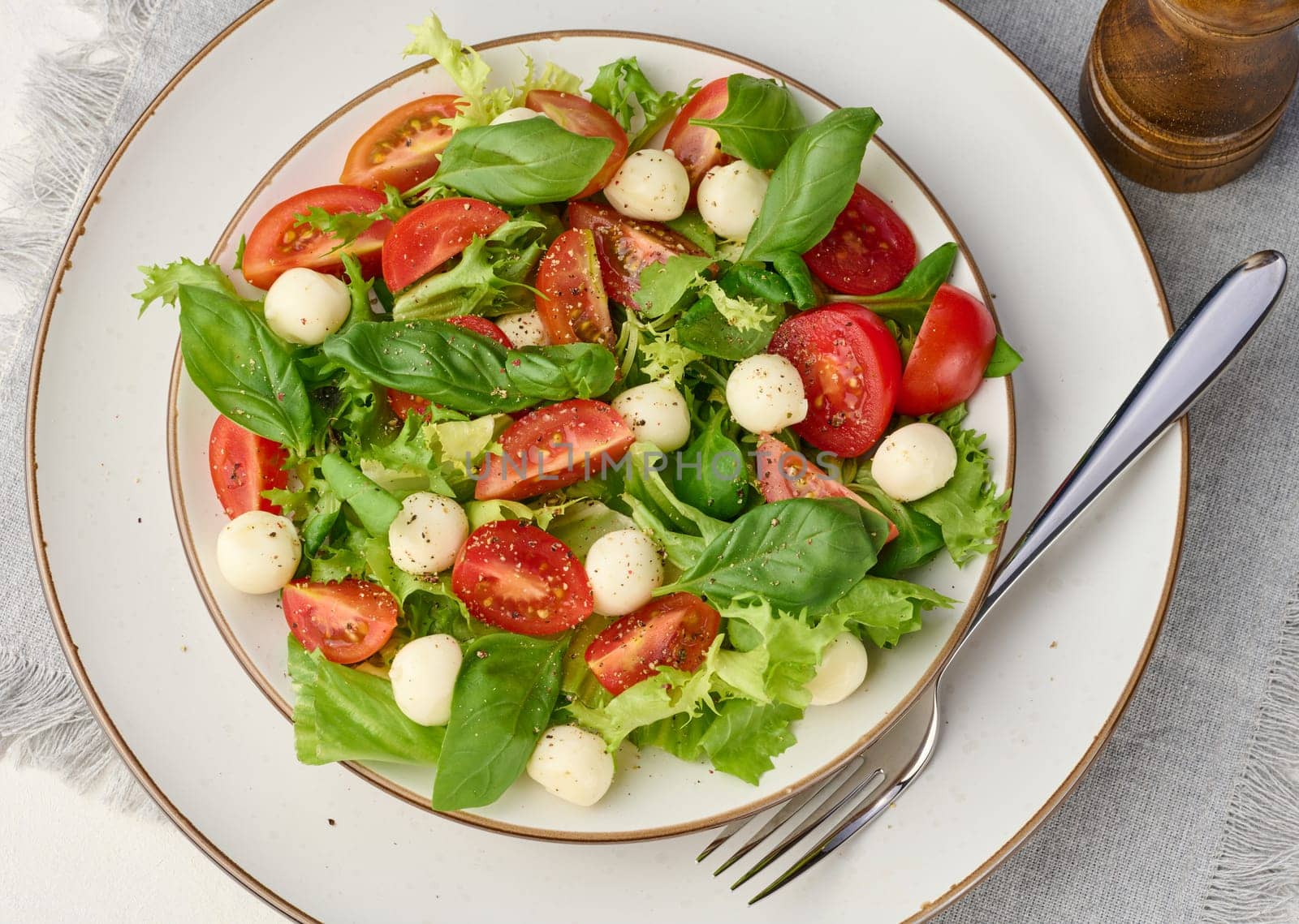 Salad with mozzarella, cherry tomatoes and green lettuce in a white round plate on the table. Top view