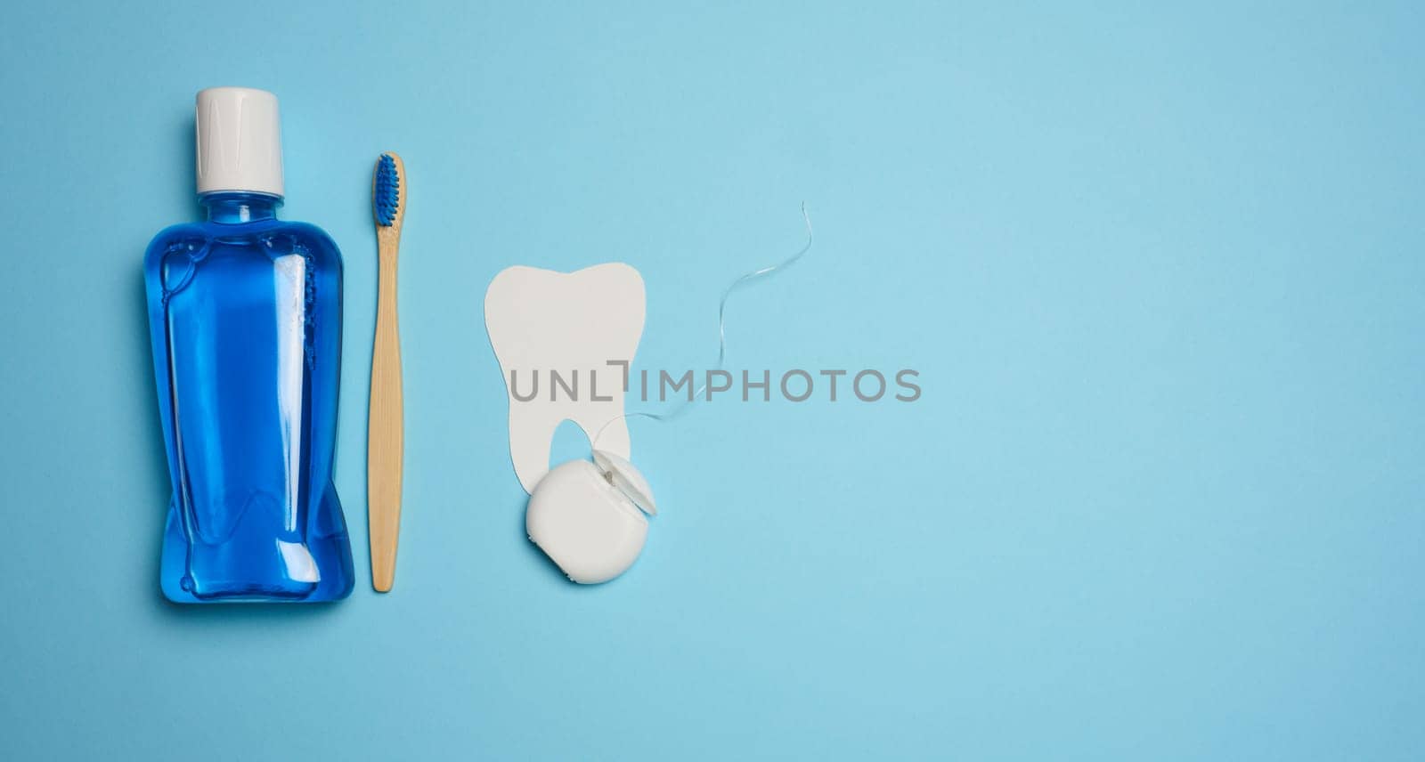 Plastic bottle with mouthwash, wooden toothbrush on blue background by ndanko