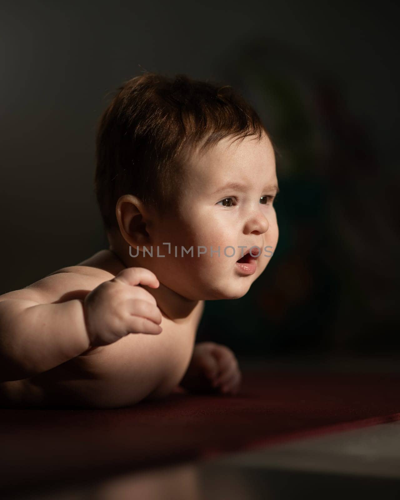 A cute little boy lies on his forearms on the floor. Vertical photo