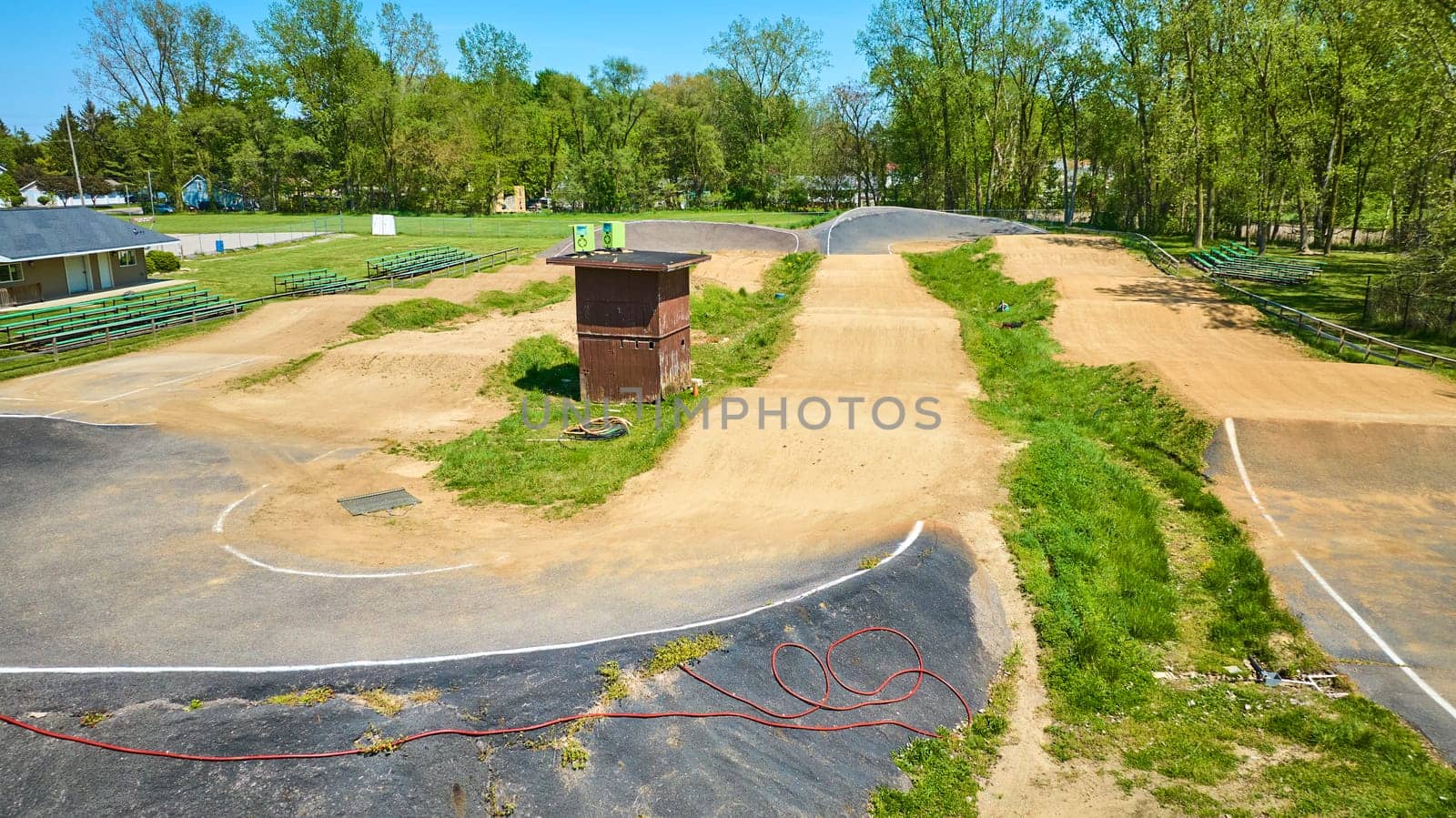 Aerial view of a sunlit BMX track in Warsaw, Indiana, featuring ramps, a judge's booth, and spectator bleachers.