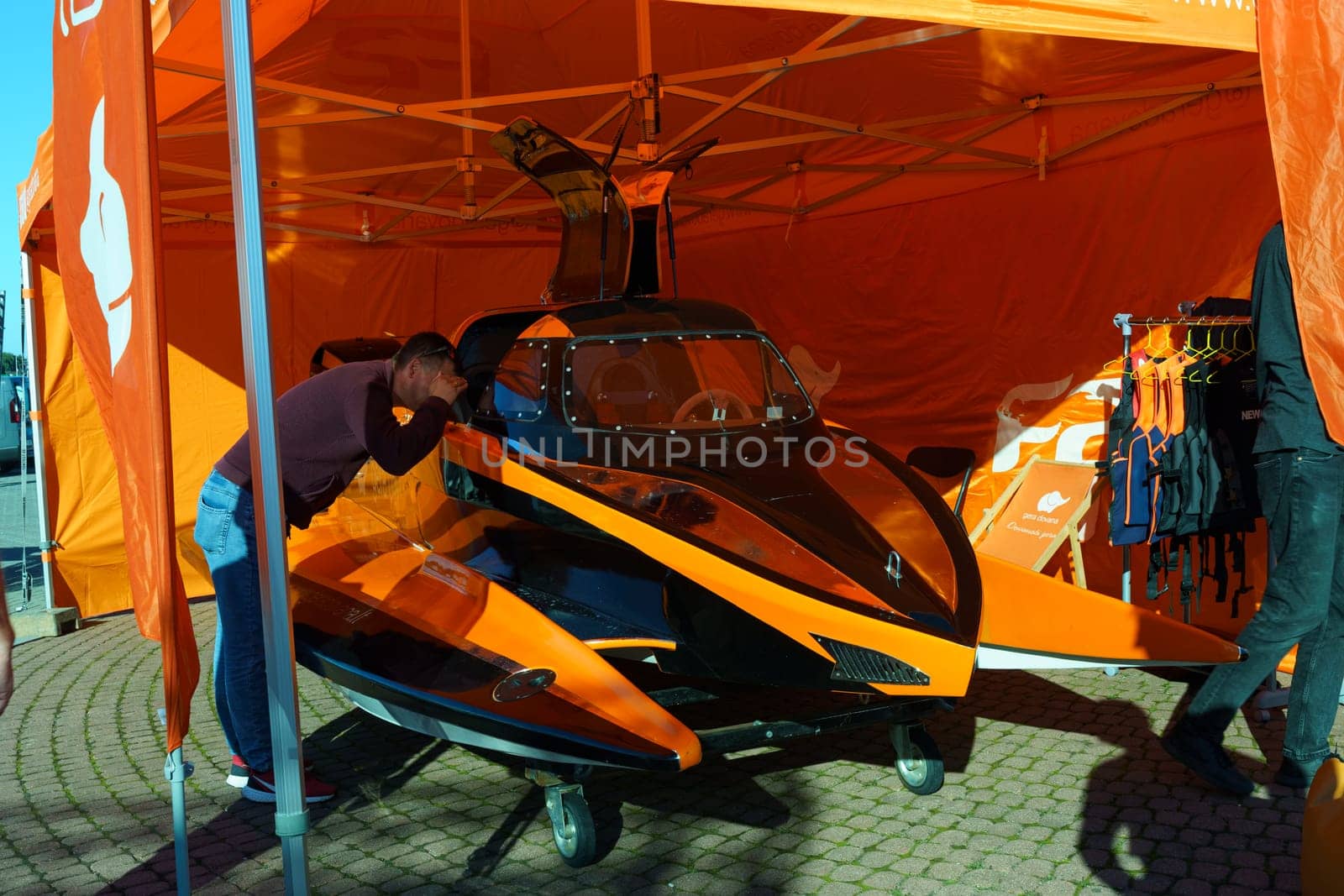 Klaipeda, Lithuania - August 11, 2023: A man in casual clothing standing next to a vibrant orange and black jet ski on a sandy beach.
