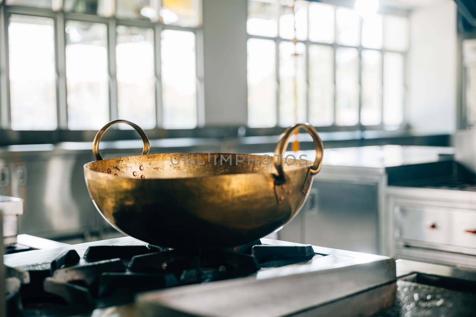 Shiny metal bowl occupies stove in a professional kitchen of a modern restaurant. Clean arrangement of chrome appliances equipment and new furniture. Bright gas service is working. by Sorapop