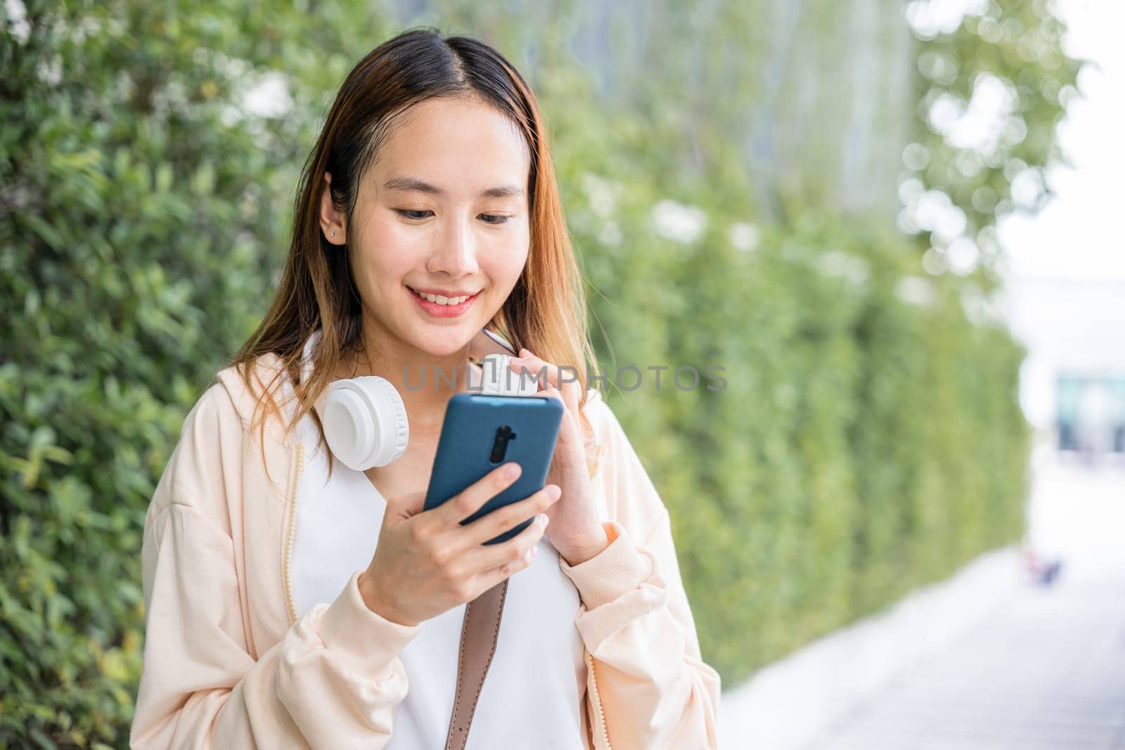 Amidst the beauty of an urban city garden a relaxed young woman uses wireless headphones to choose and listen to her favorite music. Her joyful dance in bright season adds to the vibrant atmosphere.