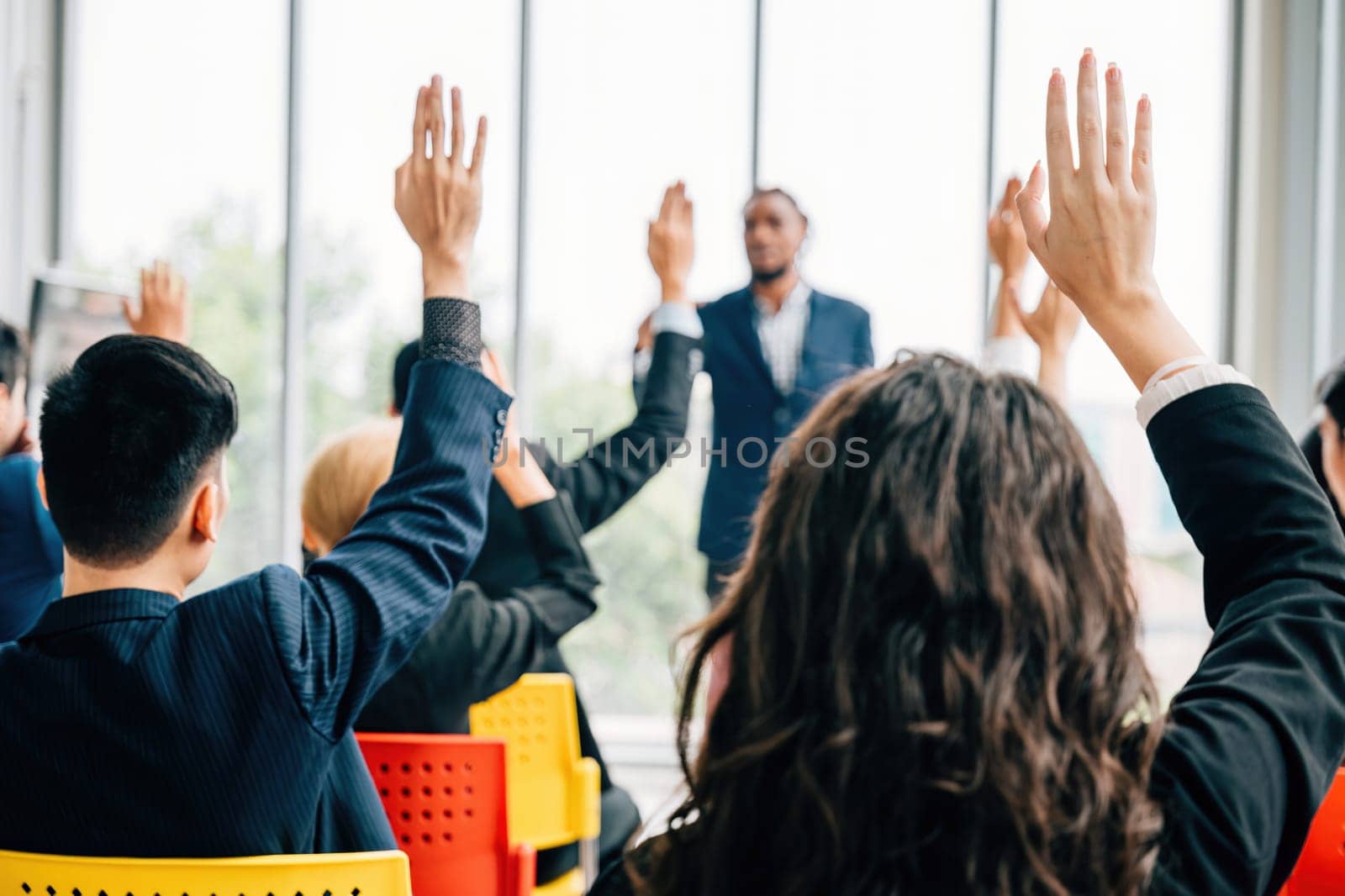 At a corporate event businesspeople engage in a conference and convention. Hands are raised symbolizing questions and active participation in a meeting and training seminar. by Sorapop