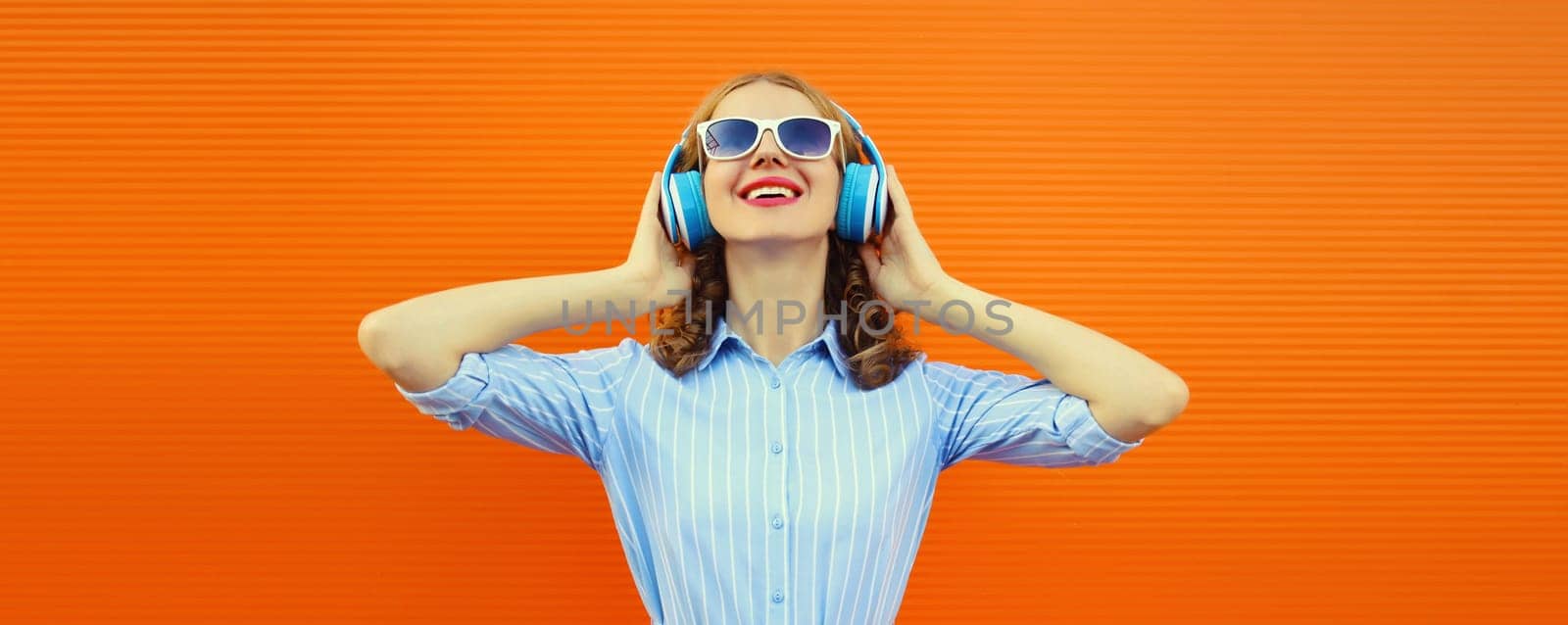 Happy modern happy young woman listening to music with headphones on bright orange background by Rohappy