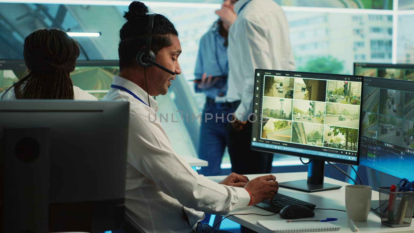 Indian employee communicating satellite map directions in observation room, monitoring traffic around the city via CCTV security system. Young man works with video surveillance data. Camera A.