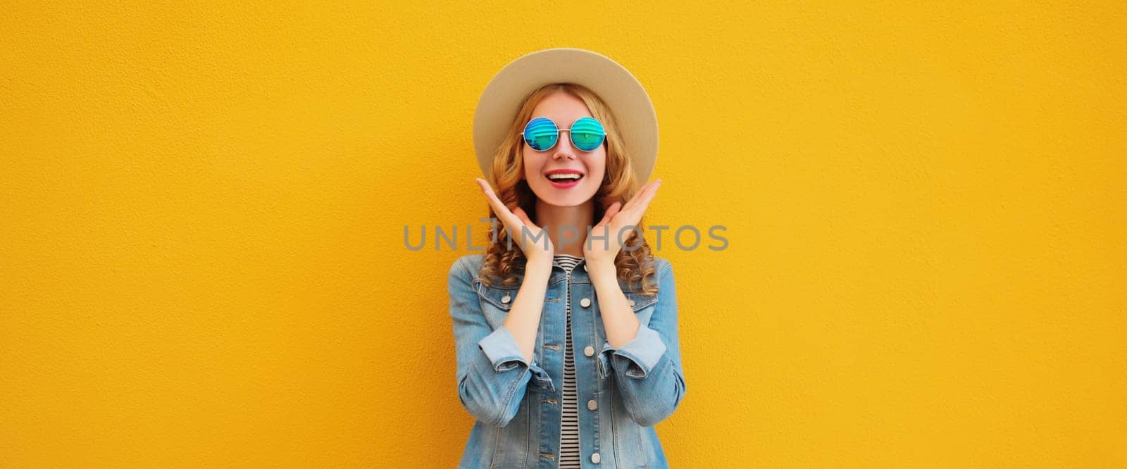 Portrait of stylish happy surprised young woman wearing summer straw hat, glasses posing on orange background