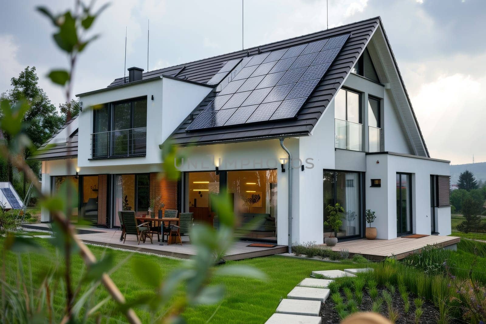 A large house with a lot of windows and a solar panel on the roof. The house is surrounded by a lush green lawn and a garden. The house has a modern and eco-friendly design
