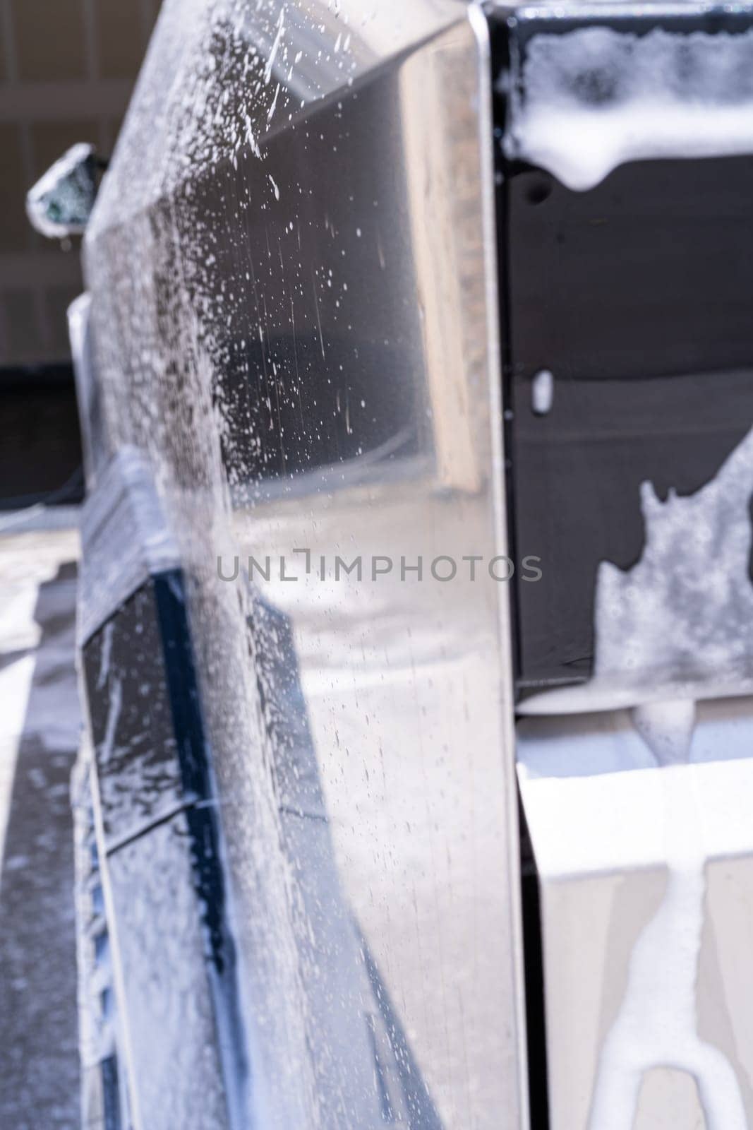 Denver, Colorado, USA-May 5, 2024-This image captures a detailed view of soap suds accumulating and dripping off the edge of a Tesla Cybertruck window during a wash, highlighting the vehicle distinct, clean lines and reflective surfaces.