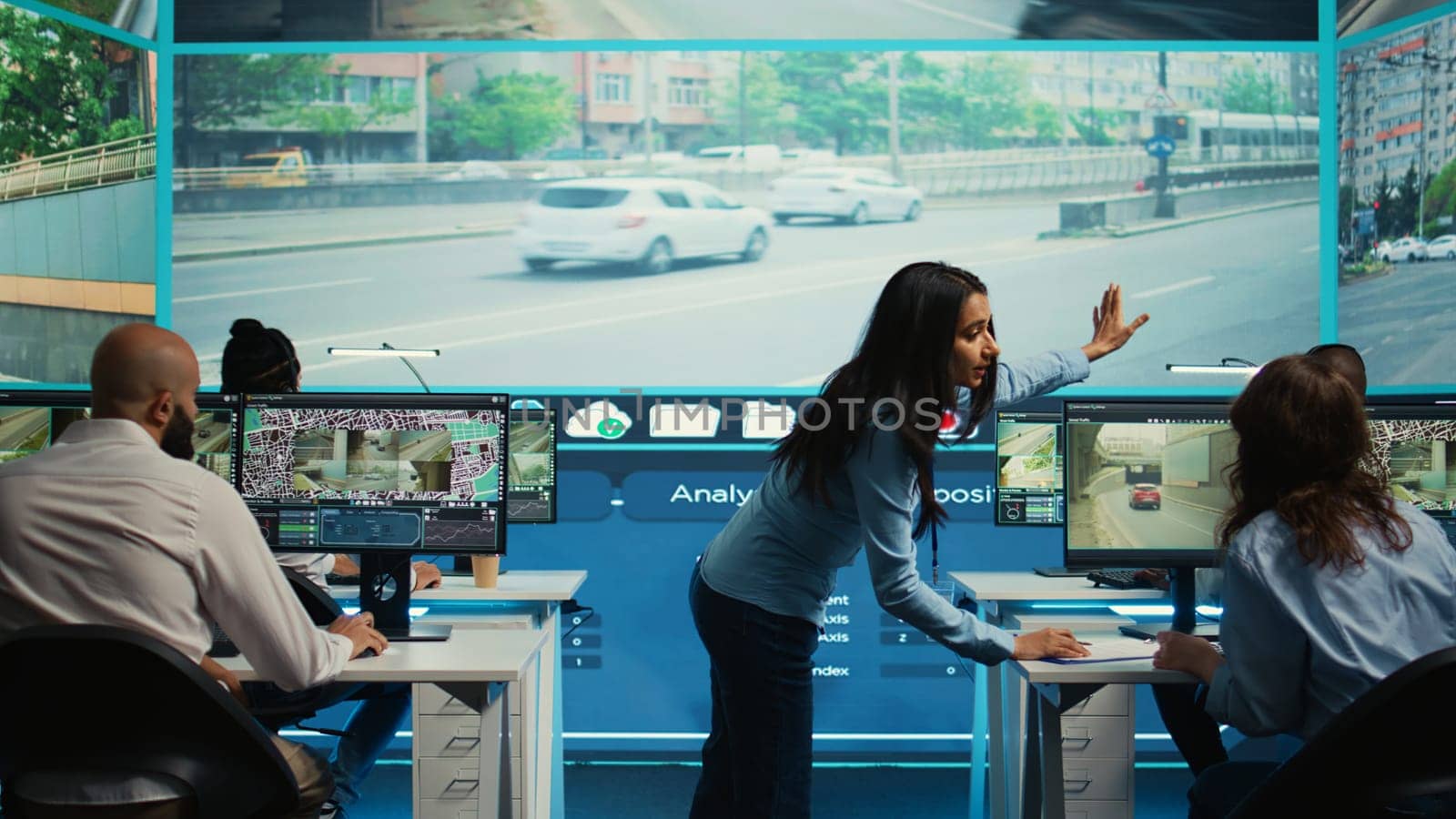 Indian supervisor leads her team to monitor the surveillance video footage and CCTV cameras to learn about urban traffic dynamics. Diverse people working on public safety. Camera B.