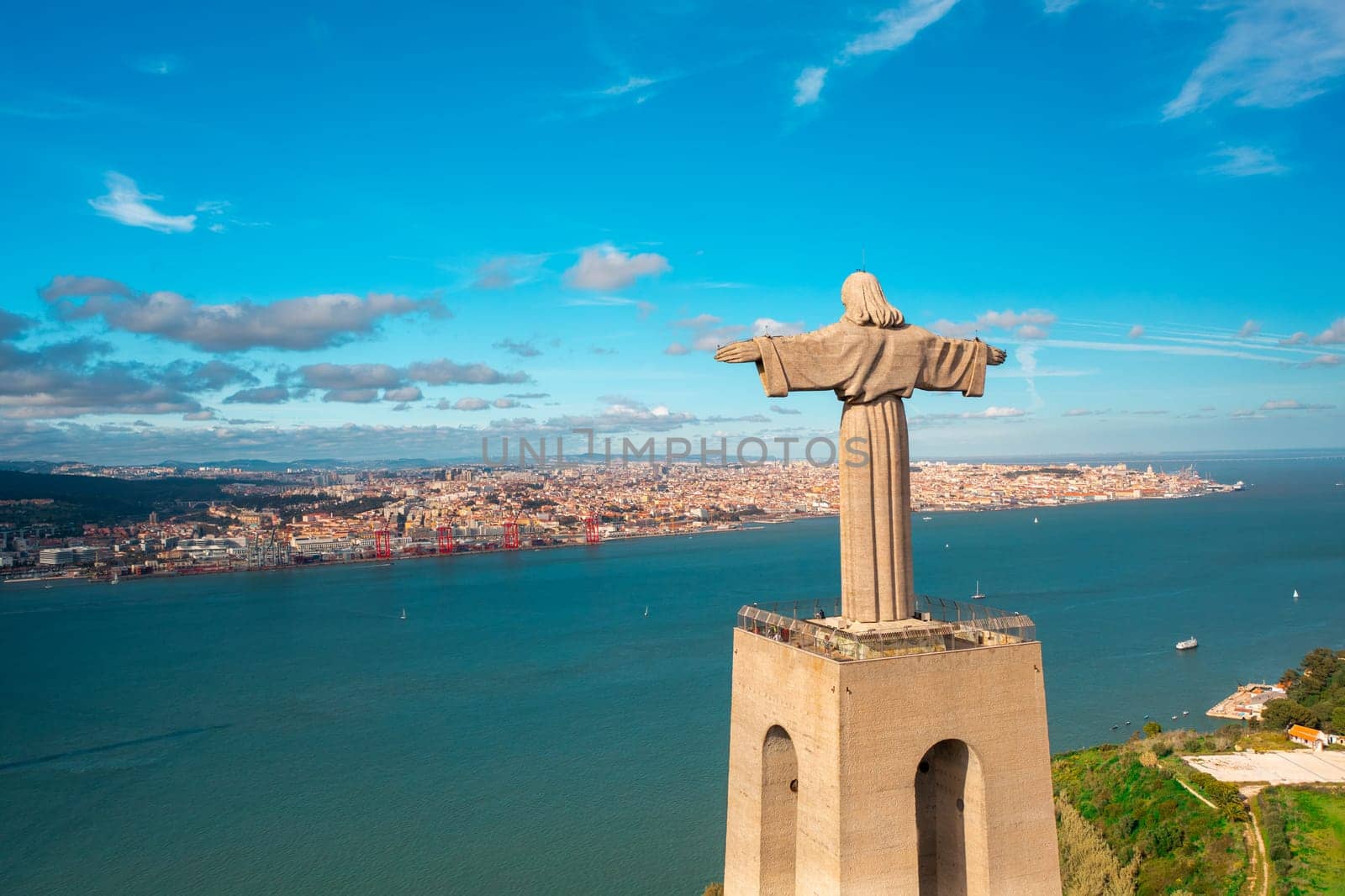 Aerial View of Christ the King Statue overlooking Tagus River and cityscape under blue sky. Bird's eye view Catholic monument and city. Lisbon, Portugal