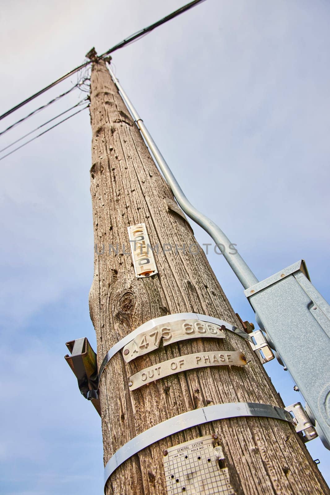 Aging utility pole in Fort Wayne, marked with hazard warnings, under a cloudy sky, symbol of enduring connectivity.