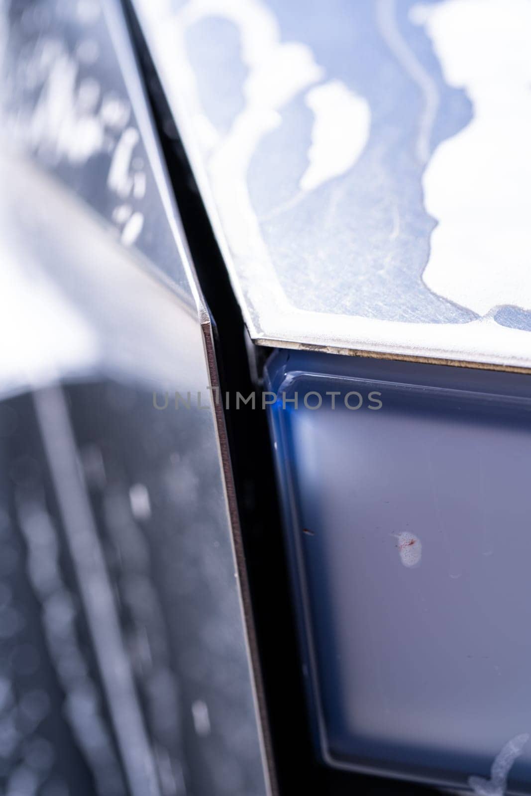 Denver, Colorado, USA-May 5, 2024-This image captures a detailed close-up of a Tesla Cybertruck sleek exterior, showcasing the edge where the body meets the window, highlighted by soap suds and water during a cleaning session. The angular design and reflective surface emphasize the futuristic style of the vehicle.