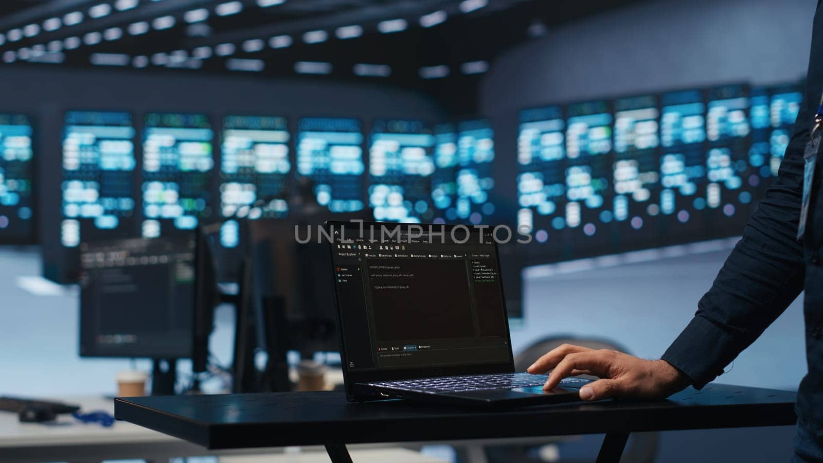 IT support employee writing code on laptop in high tech facility with server rows providing computing resources for different workloads. System administrator uses notebook to oversee supercomputers