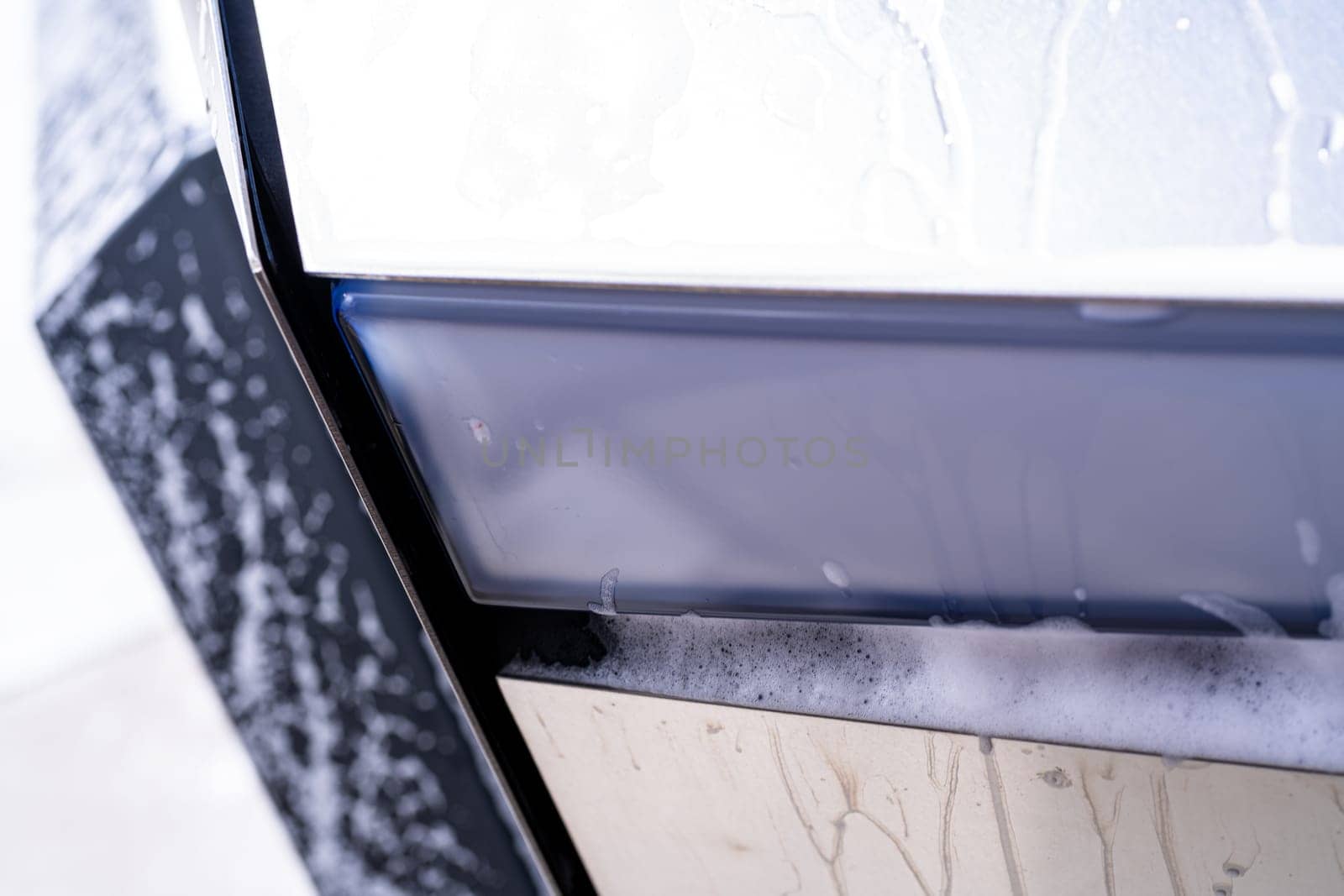 Denver, Colorado, USA-May 5, 2024-This image captures a detailed close-up of a Tesla Cybertruck sleek exterior, showcasing the edge where the body meets the window, highlighted by soap suds and water during a cleaning session. The angular design and reflective surface emphasize the futuristic style of the vehicle.