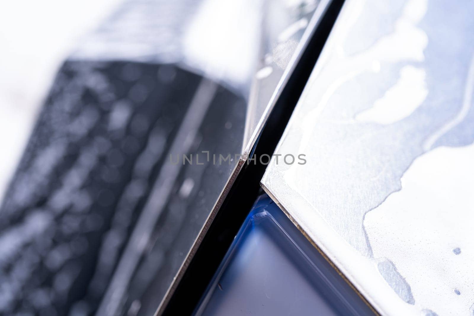 Denver, Colorado, USA-May 5, 2024-This image captures a detailed close-up of a Tesla Cybertruck sleek exterior, showcasing the edge where the body meets the window, highlighted by soap suds and water during a cleaning session. The angular design and reflective surface emphasize the futuristic style of the vehicle.